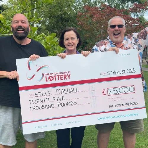 Steve from Leamington smiling in his garden, holding the cheque presentation card from the July draw